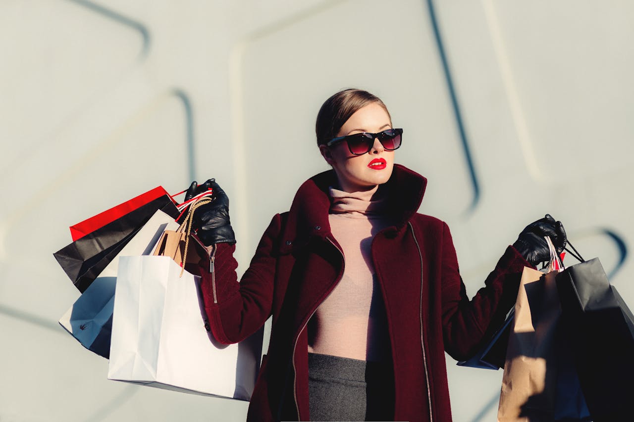 programs-03 Stylish young woman in sunglasses carrying shopping bags outdoors. Elegant fashion statement.