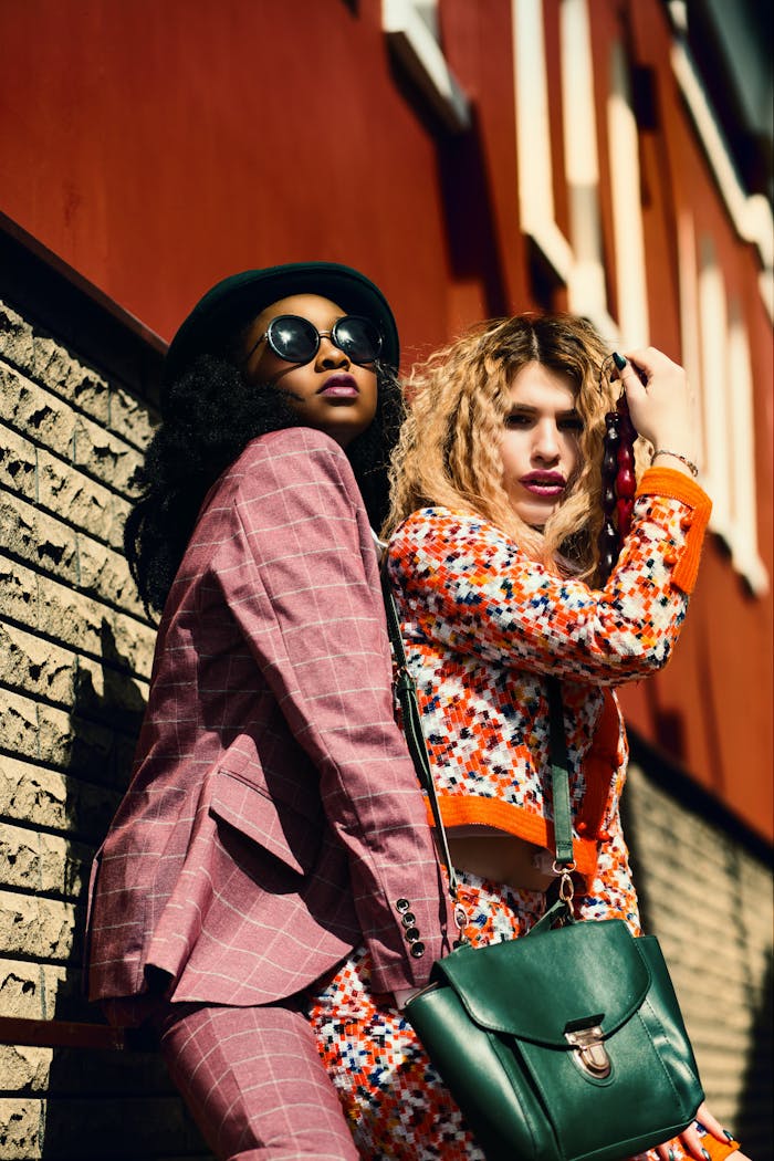 programs-01 Two fashionable women posing stylishly against an urban background, showcasing vibrant outfits and accessories.